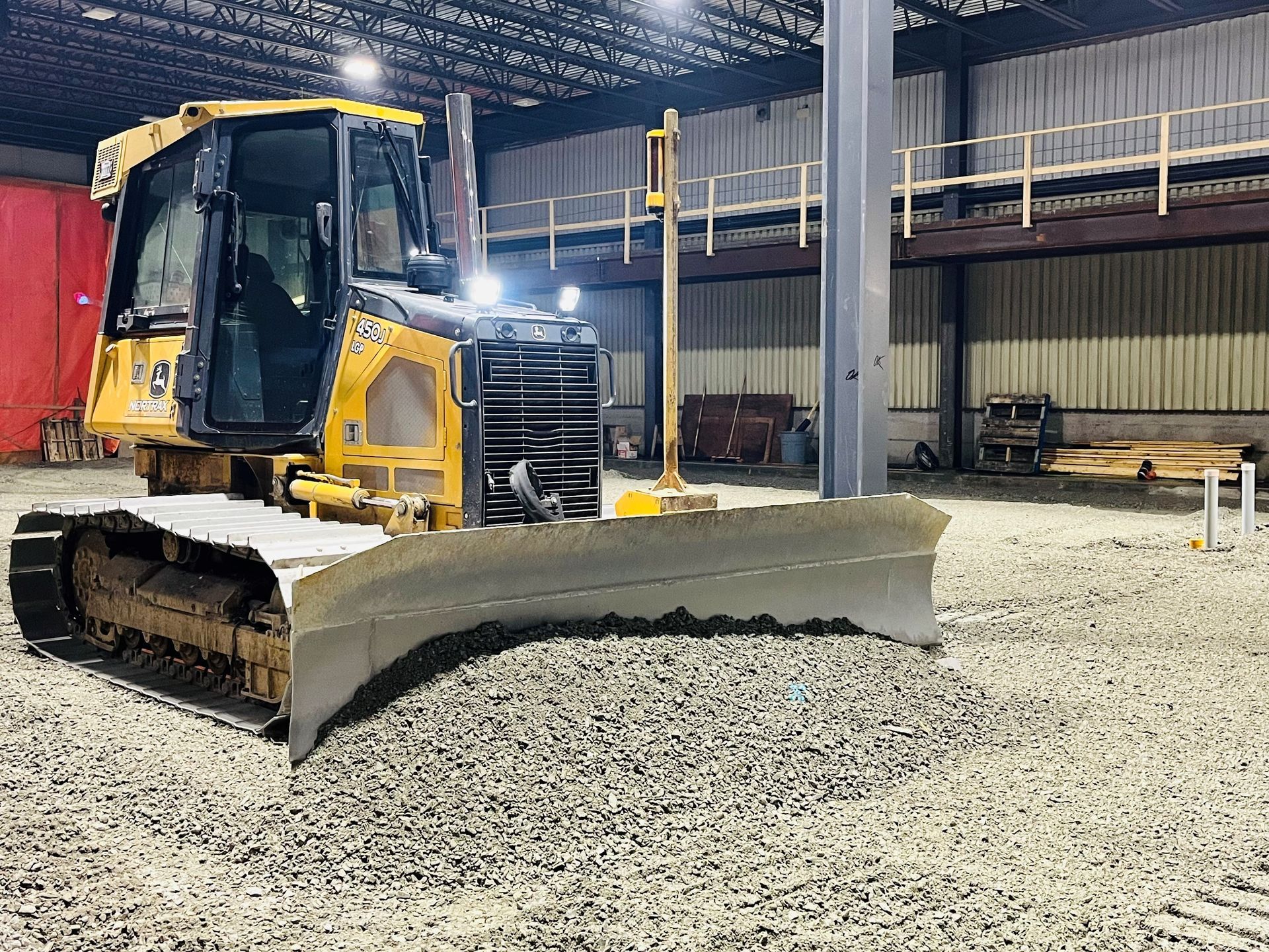Bulldozer jaune avec une lame stationné sur du gravier à l'intérieur d'un entrepôt industriel éclairé la nuit