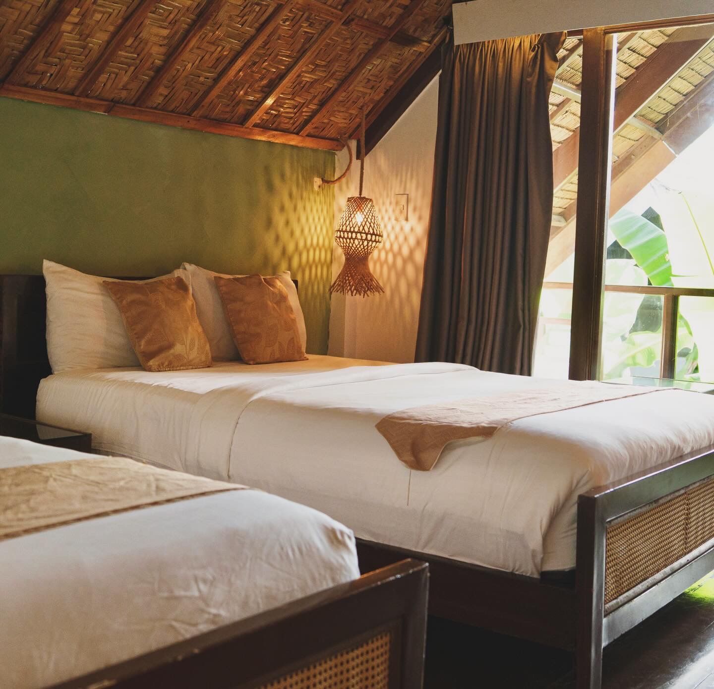 Tropical bedroom with two white beds, woven headboard, and open curtains by a window
