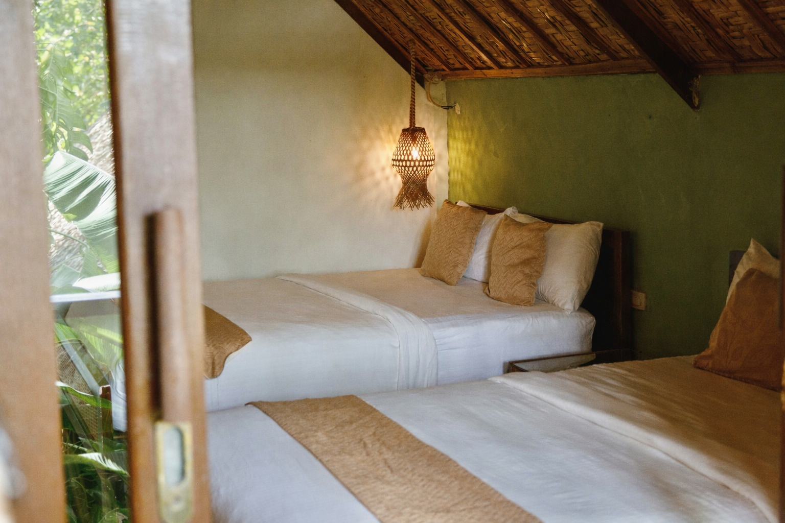 Rustic bedroom with two white beds, tan accents, and a hanging lantern under a sloped wooden ceiling