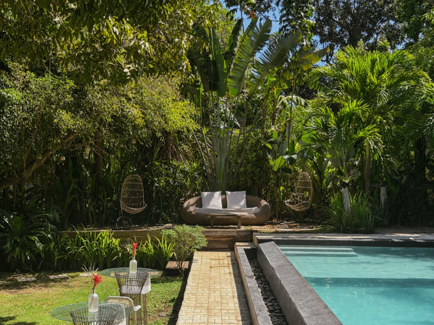 Tropical backyard patio with pool, stone path, and cushioned seating amid lush greenery