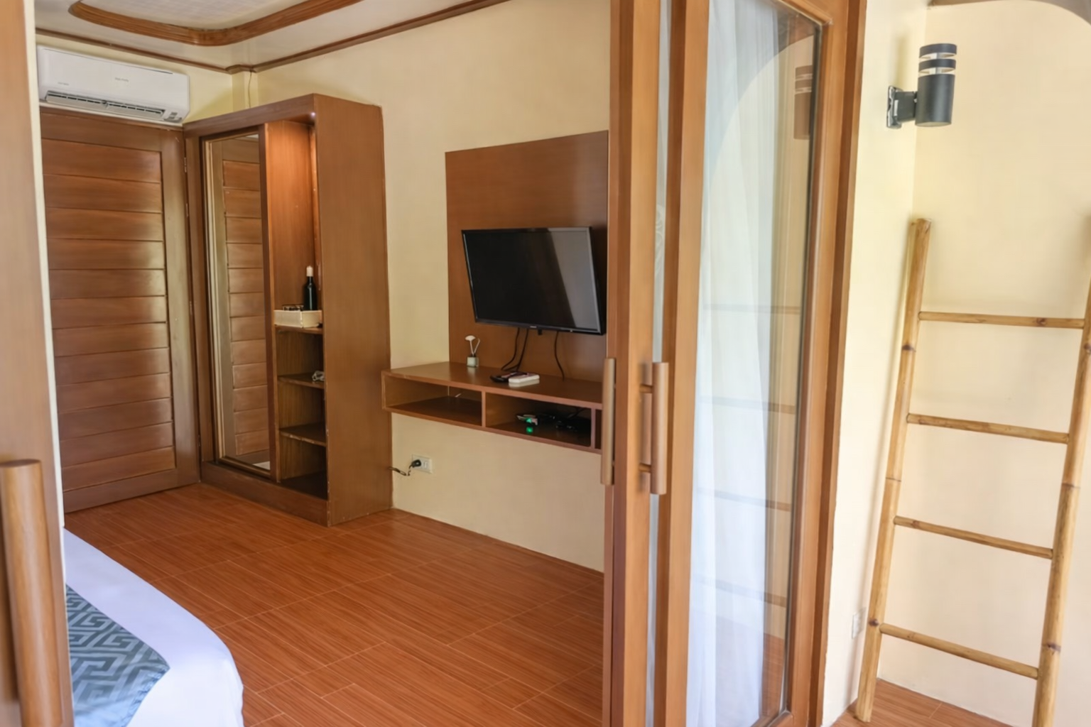 Bedroom with wood-paneled walls, TV on a wall unit, wardrobe, and ladder shelf by a doorway.