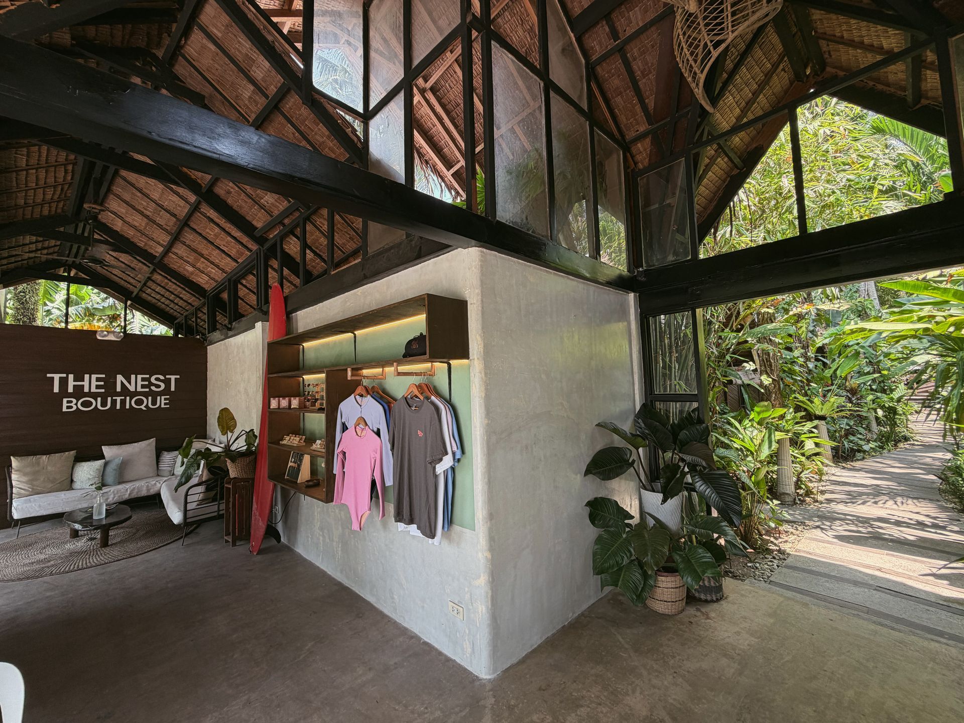Boutique-style lodge interior with hanging clothes, seating, plants, and a view of greenery outside
