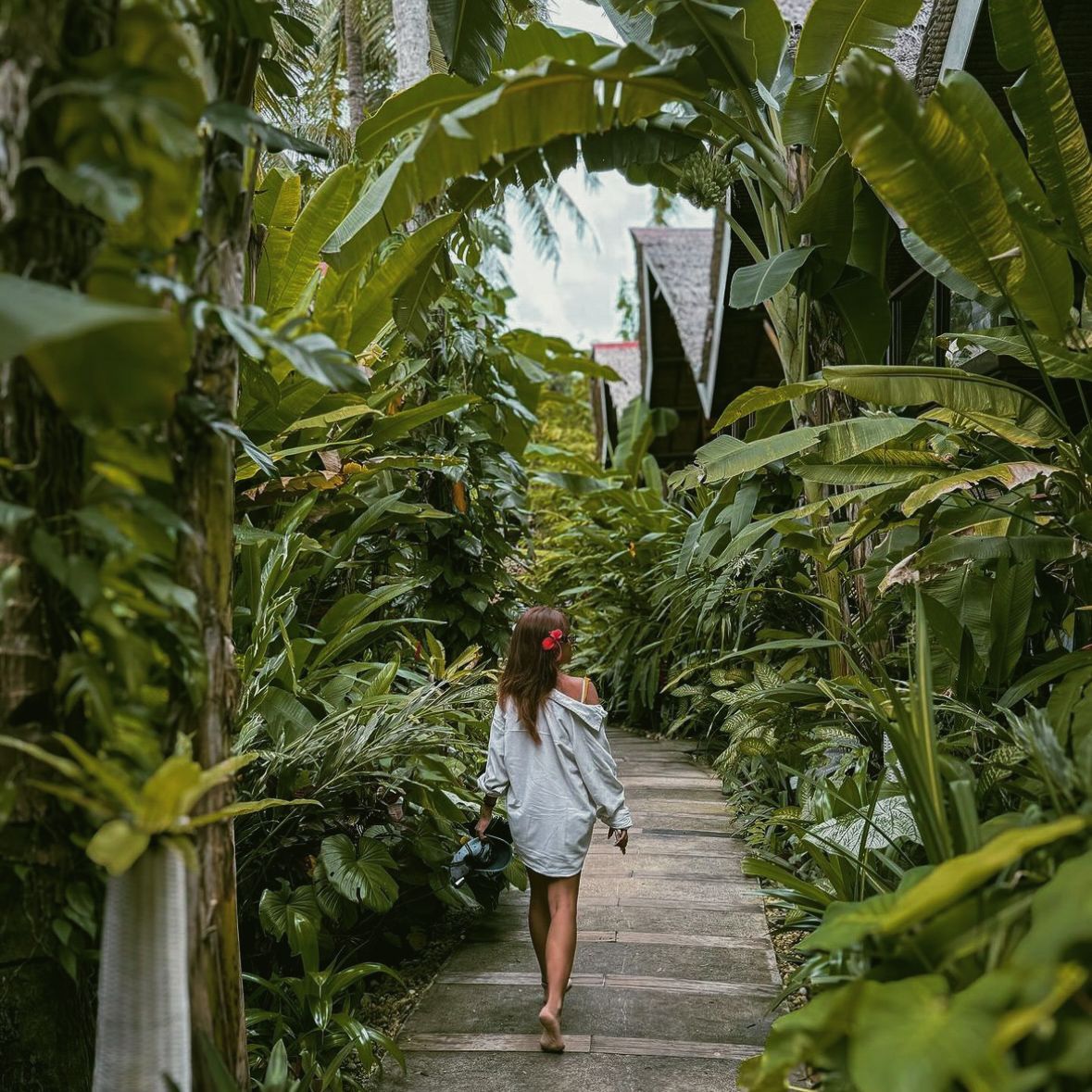 Woman walking along a narrow stone path through lush tropical greenery