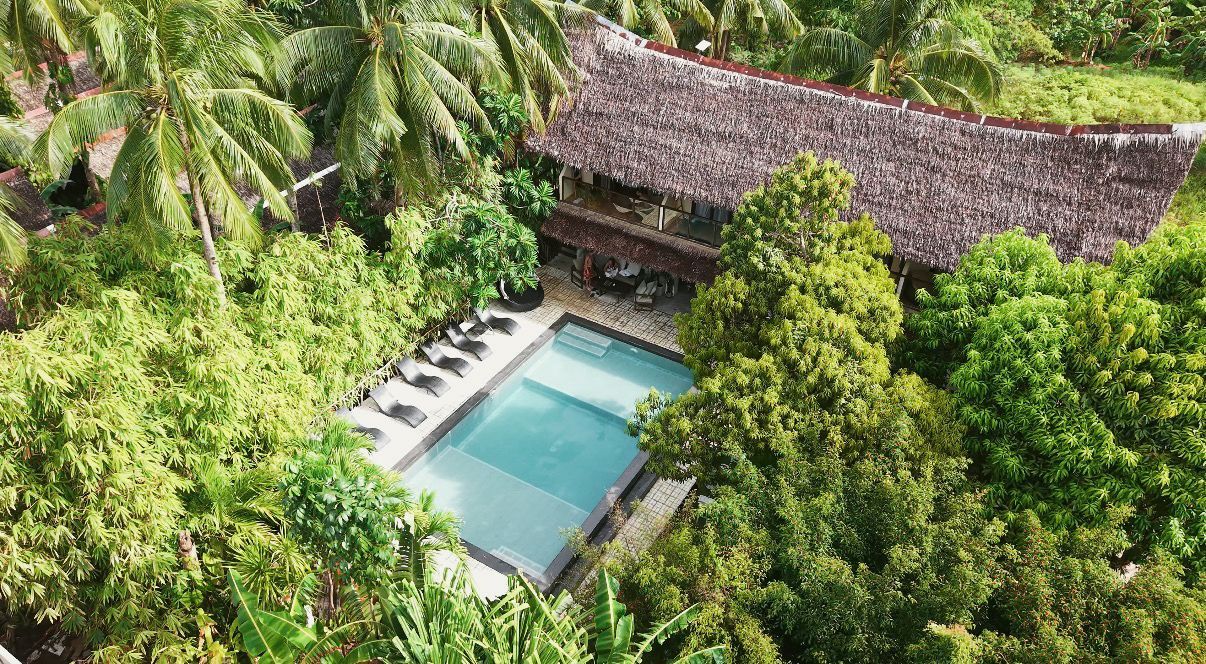 Aerial view of a tropical villa with a blue pool surrounded by lush green palms and trees