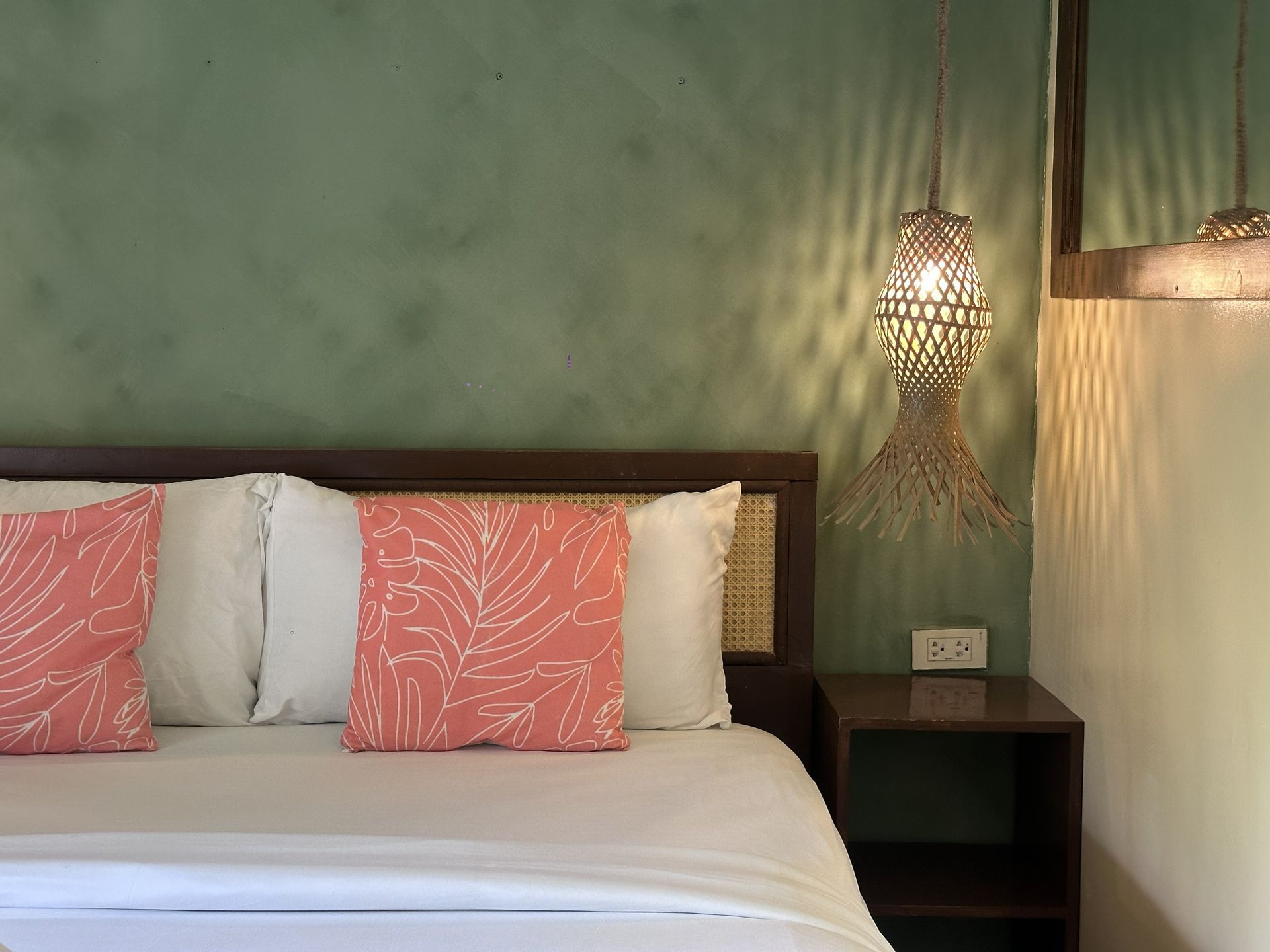 Cozy bedroom with white bed, pink pillows, and a woven hanging lamp beside a nightstand