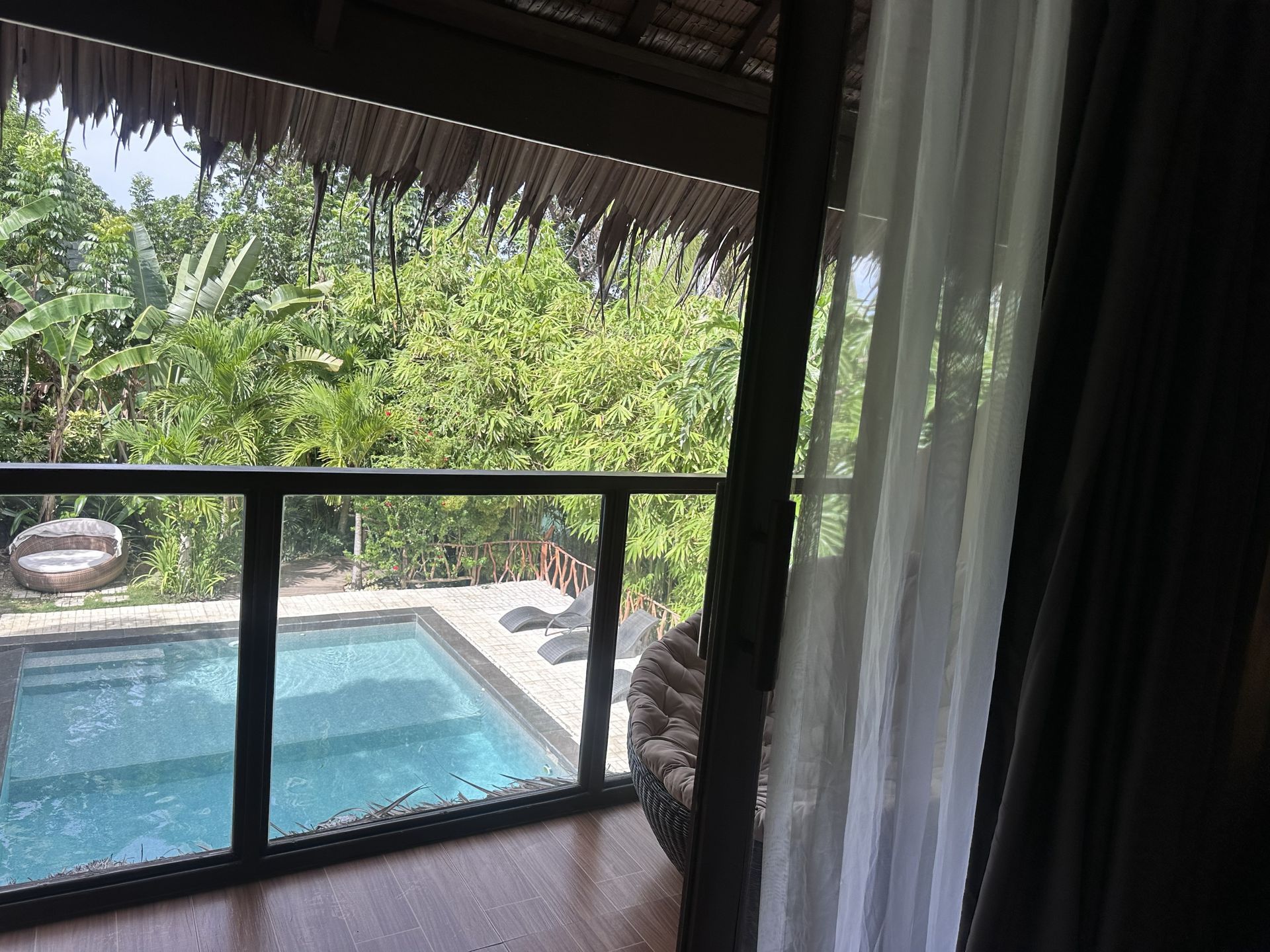 Covered patio overlooking a small blue pool and lush tropical garden through a glass railing