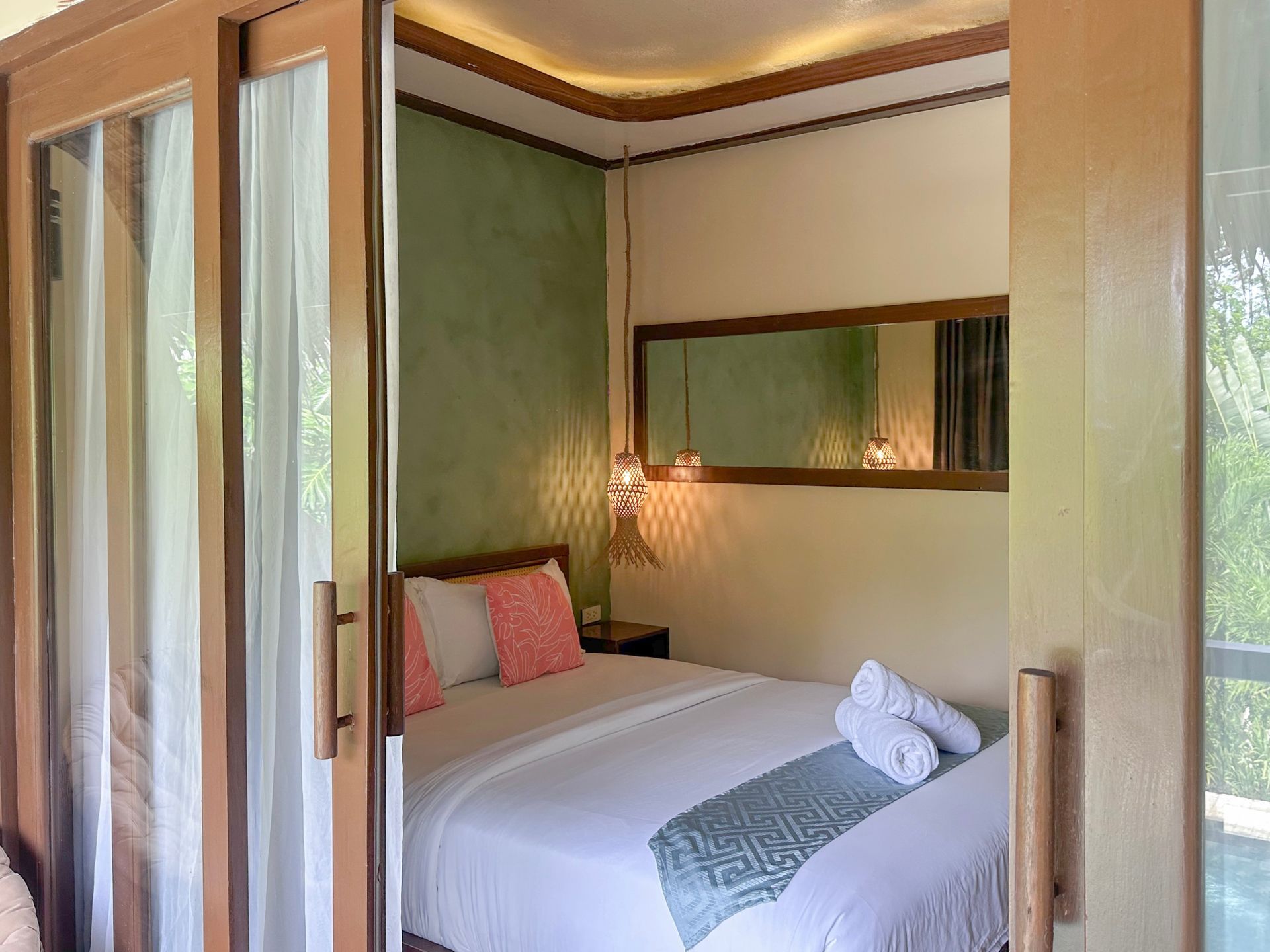 Cozy bedroom with green walls, a white bed, wooden accents, and a folded towel at the foot.