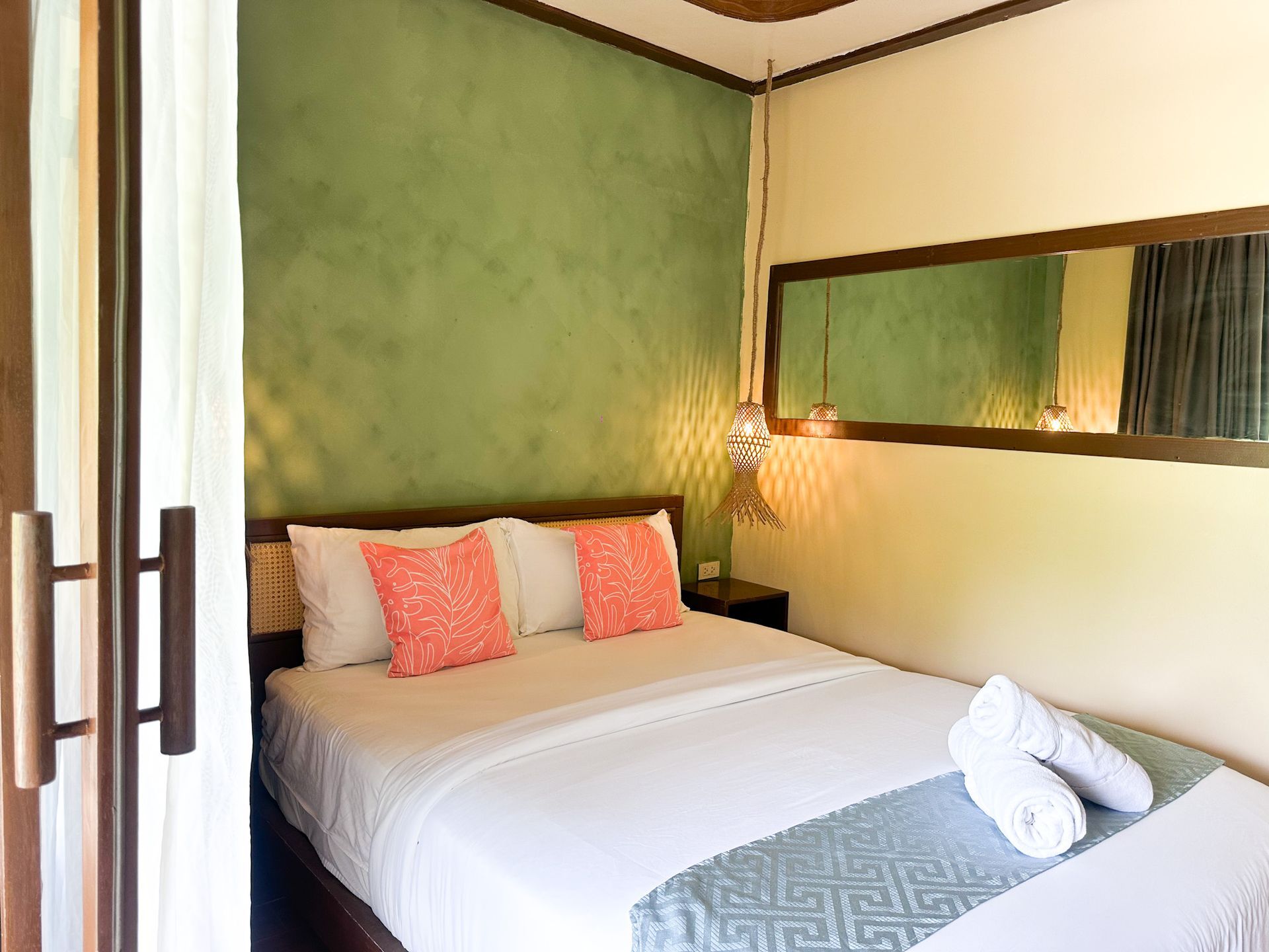 Cozy bedroom with green accent wall, white bed, coral pillows, and a wall mirror