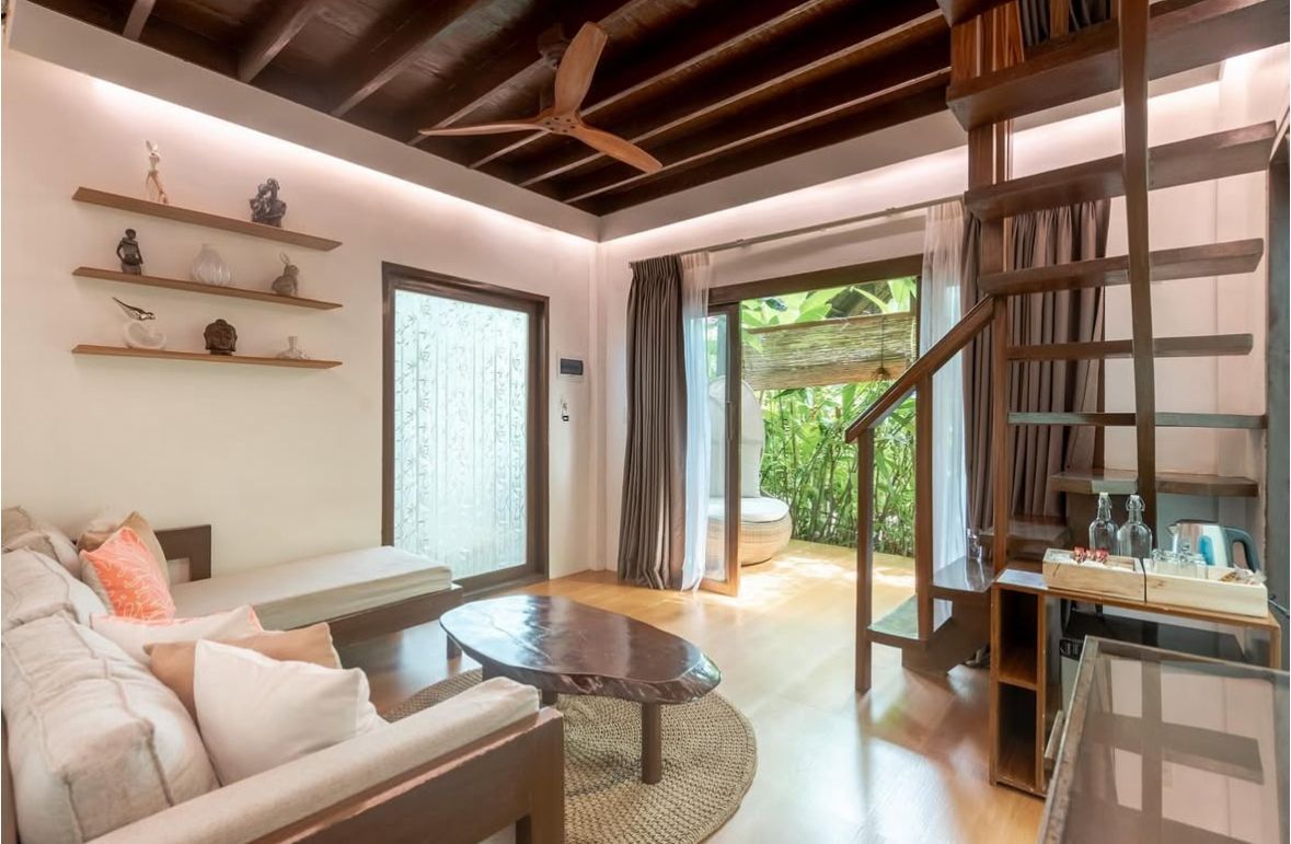 Bright living room with sofa, glass coffee table, staircase, and open patio doors to a green garden