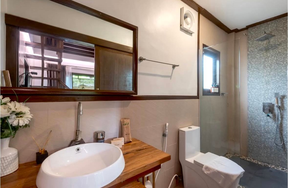 Modern bathroom with wood vanity, round sink, mirror, toilet, and walk-in shower with tiled walls.