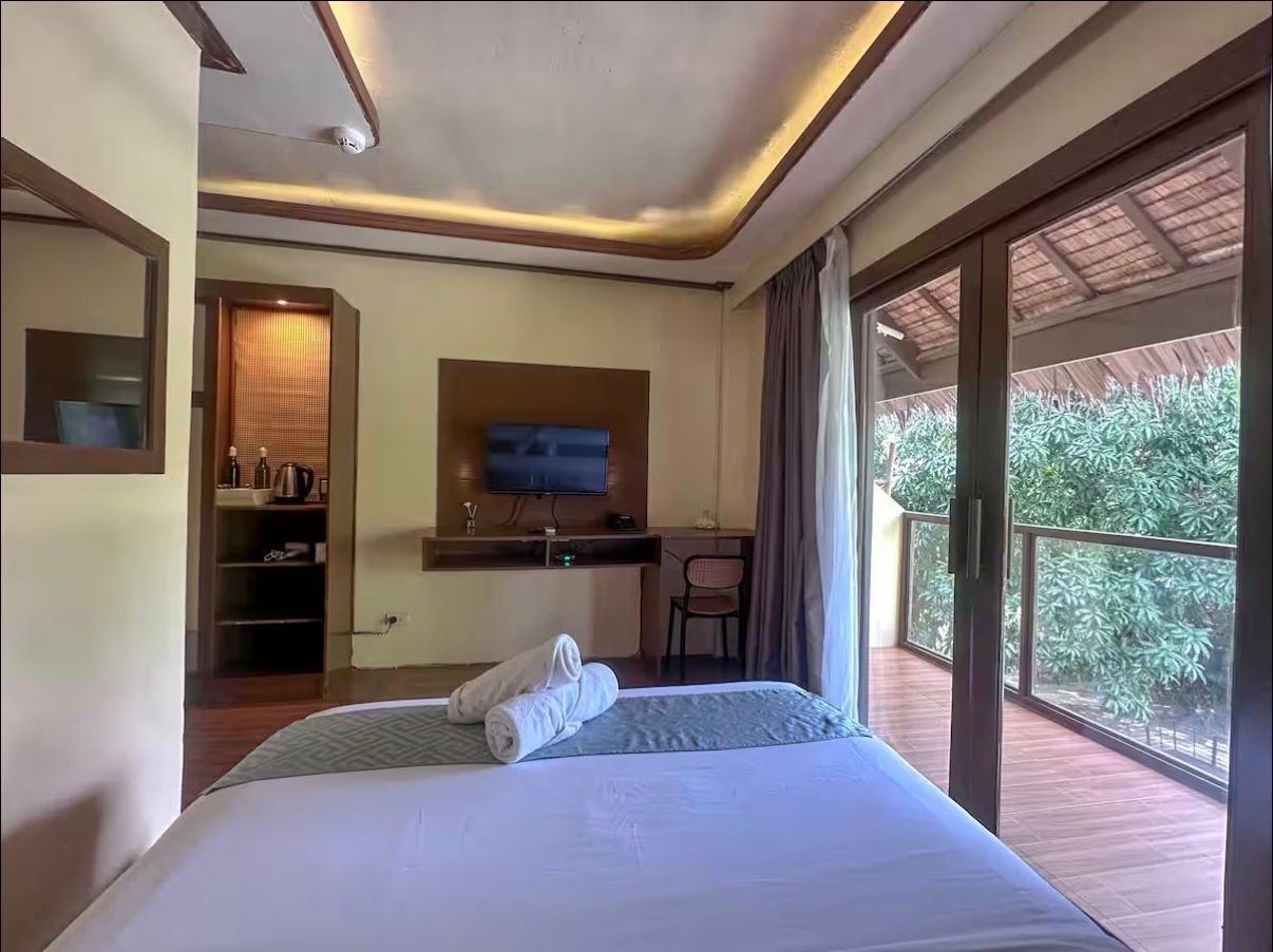 Bedroom with white bed, TV console, and sliding glass doors opening to a balcony and greenery