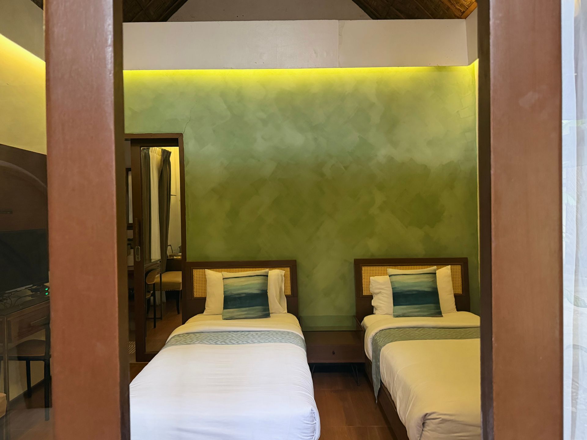 Two twin beds in a small room with green walls, warm overhead lighting, and wooden trim.