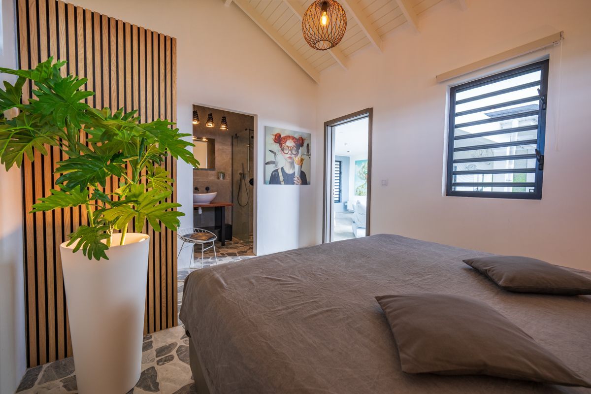 Slaapkamer met houten accentmuur, bed en openslaande deuren naar een badkamer en een andere kamer.