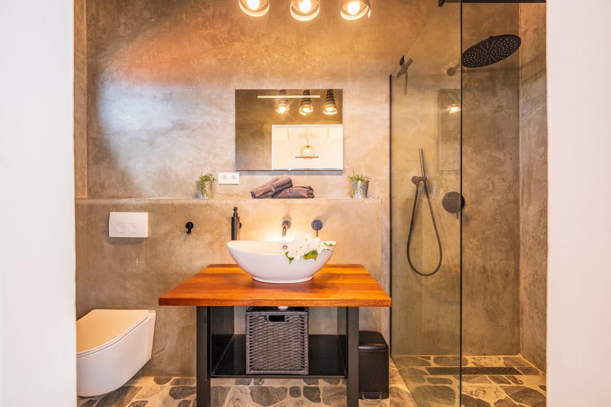 Moderne badkamer met betonnen muren, houten wastafelmeubel, opbouwspoelbak en glazen douchecabine.