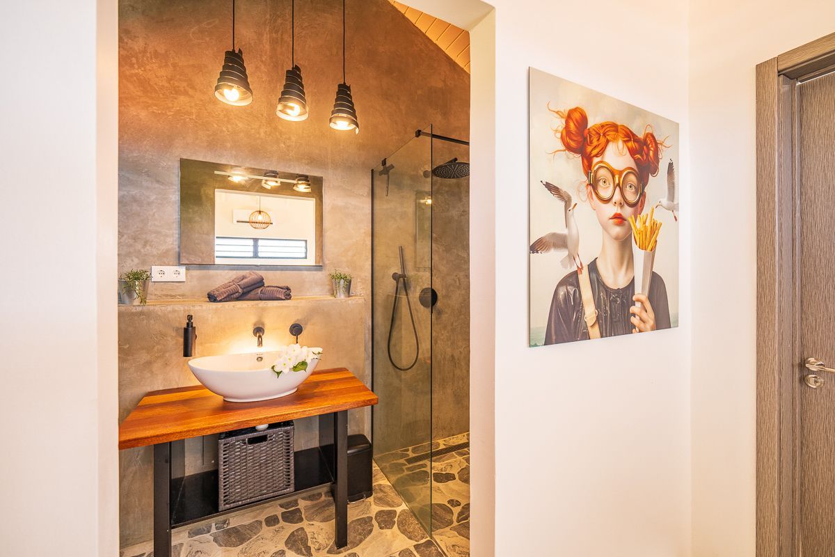 Badkamer met houten wastafelmeubel, opbouwspoelbak, inloopdouche en kunstwerk van een meisje.