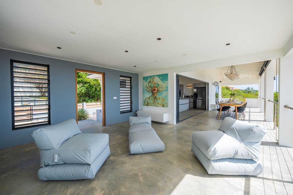 Moderne woonkamer met blauwgrijze muren, die uitkomt op een terras. Voorzien van grijze loungestoelen en abstracte kunst.