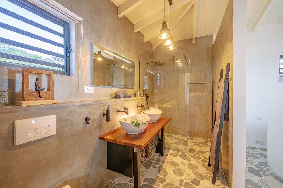 Badkamer met betonnen muren, houten wastafelmeubel, stenen vloer en glazen douchecabine.