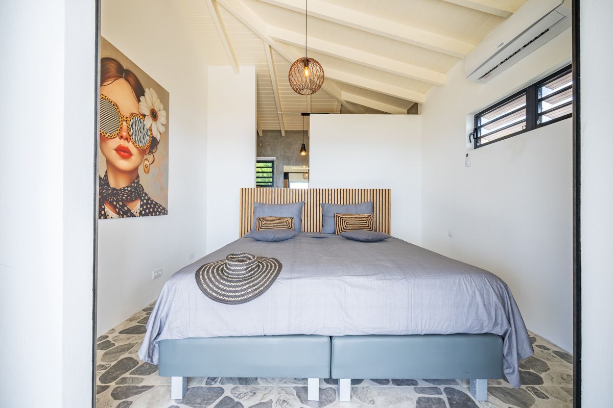 Slaapkamer met een tweepersoonsbed, kunst, een hoed en witte muren.
