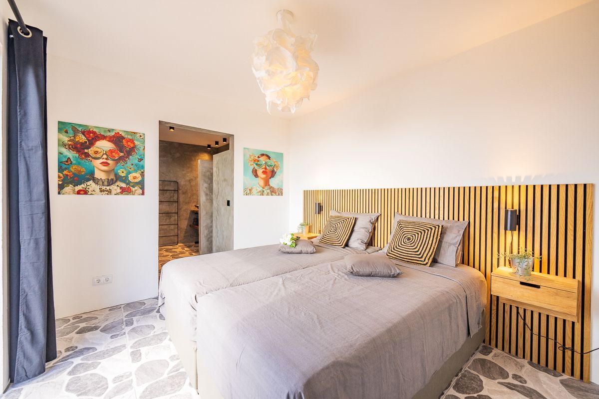 Slaapkamer met twee bedden, een decoratief hoofdeinde, kunst aan de muren en een vloer met een patroon.