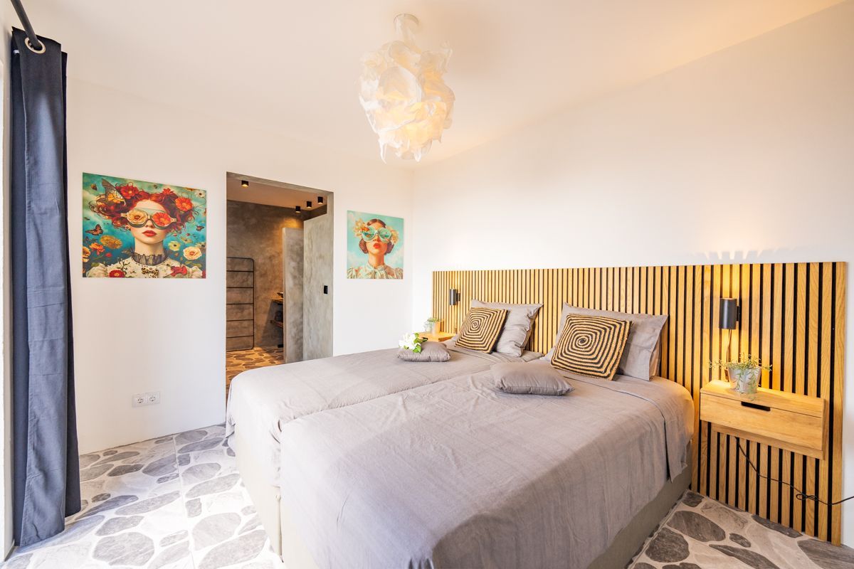 Slaapkamer met twee bedden, kunst, houten hoofdbord, klein nachtkastje en vloer met patroon.