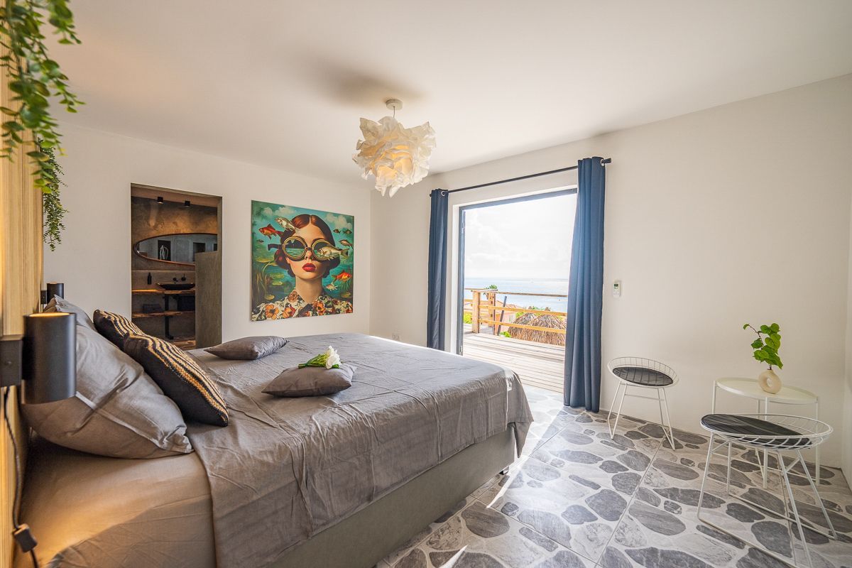 Slaapkamer met bed, kunst en balkon met uitzicht op de oceaan.