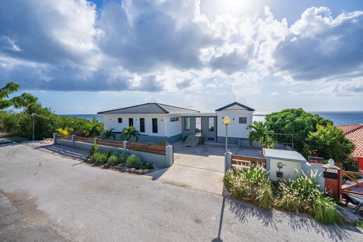 Modern wit huis met grijs dak, met uitzicht op de oceaan op een zonnige dag.