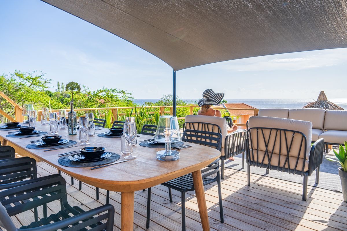 Een eethoek in de buitenlucht met een gedekte tafel en uitzicht op de oceaan.
