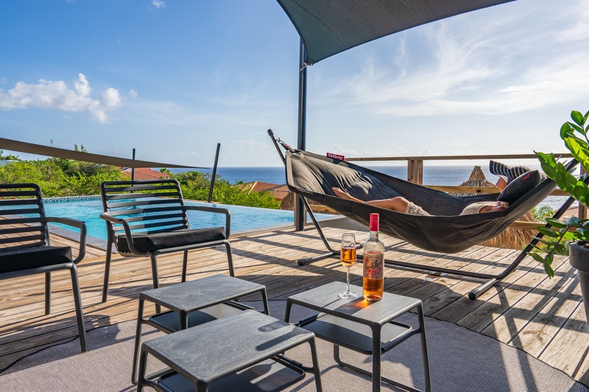 Terras met zwembad, uitzicht op de oceaan, hangmat, stoelen en een tafel met drankjes.