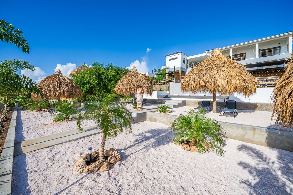 Tropisch resort met een wit gebouw, rieten parasols en een helderblauwe hemel.