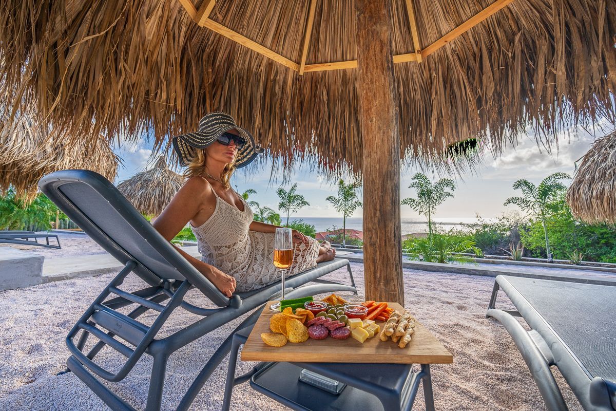 Een vrouw ontspant onder een rieten parasol en geniet van eten en drinken op het strand, op een zonnige dag.