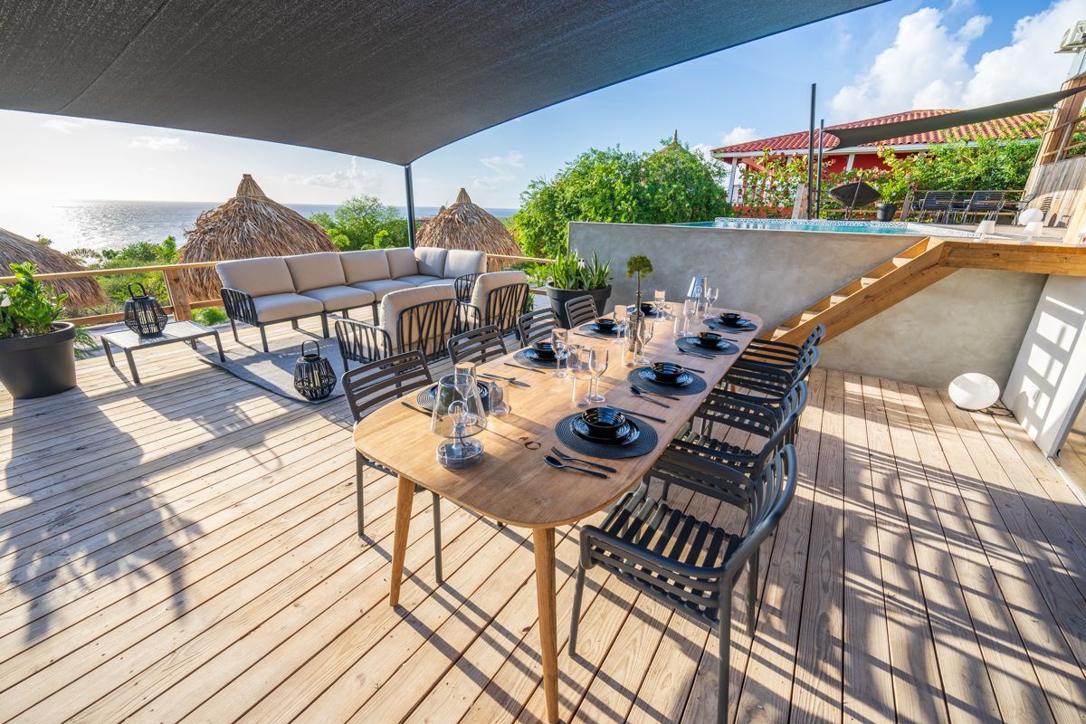 Eettafel gedekt voor gasten, met uitzicht op de oceaan op een zonnig terras.