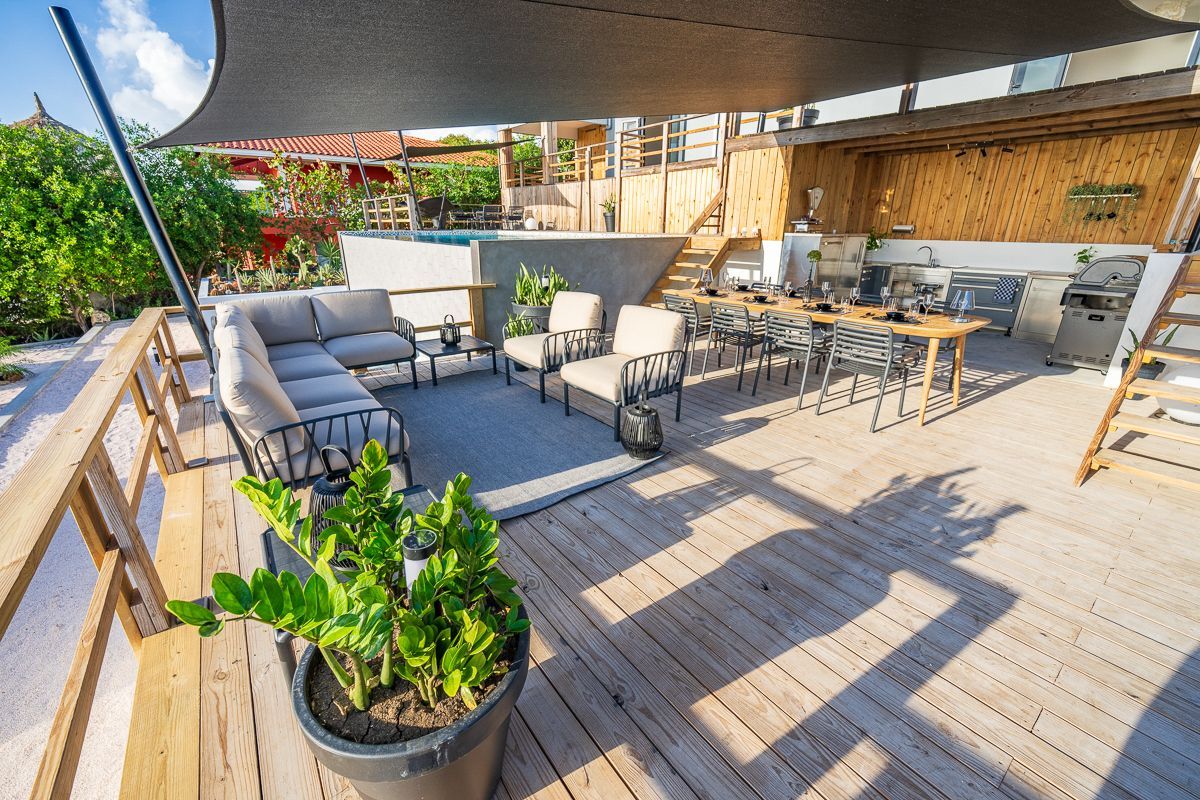 Terras met zitgelegenheid, eethoek, barbecue en schaduwdoek; zonnige dag.