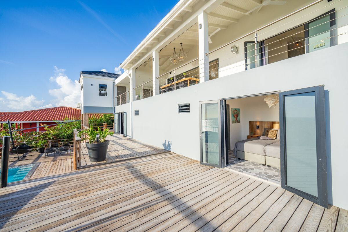 Wit, modern gebouw met houten terras en openslaande glazen deuren.