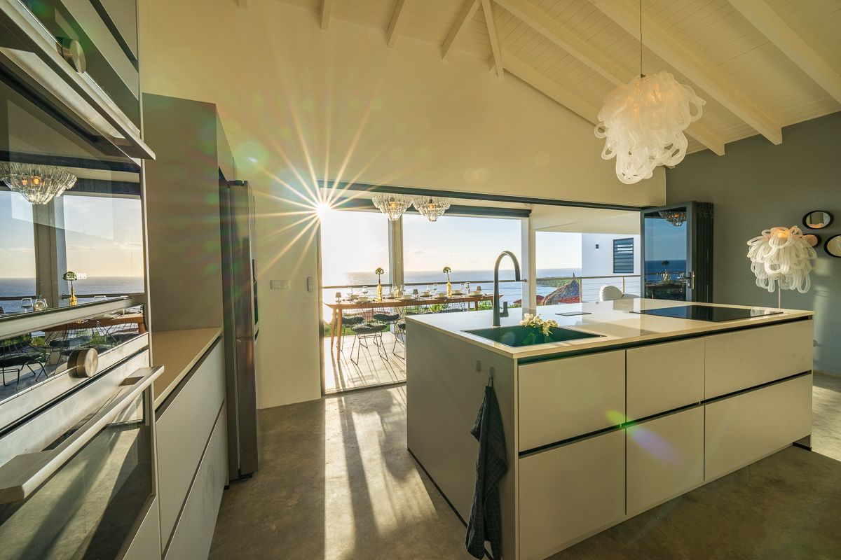 Moderne keuken met kookeiland en uitzicht op de oceaan door grote glazen deuren; veel natuurlijk licht.