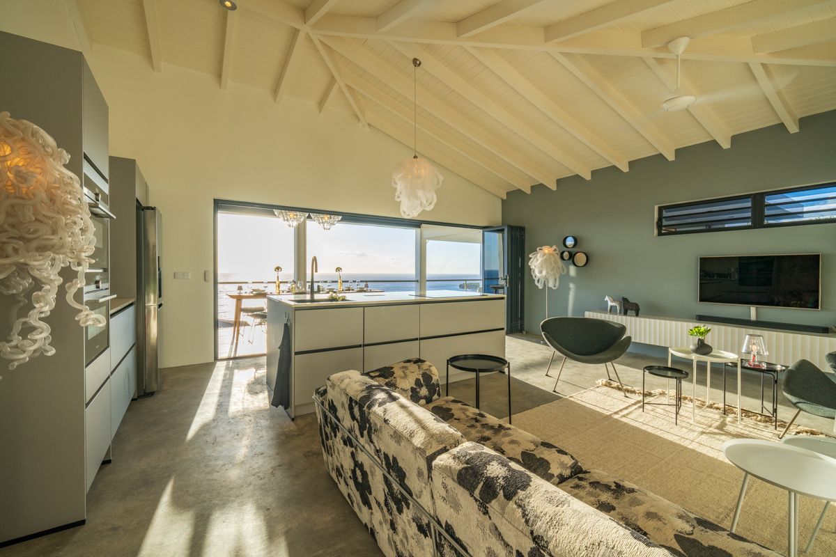 Interieur van een moderne woonruimte met uitzicht op de oceaan, grijze muren, wit plafond en eigentijds meubilair.