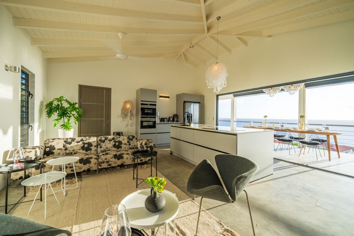Moderne open woonruimte met keuken, zithoek en uitzicht op de oceaan door een groot raam.