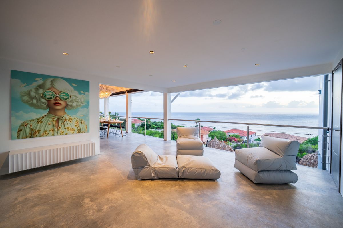 Ruime, open kamer met uitzicht op de oceaan, moderne kunst en meubilair in neutrale tinten.