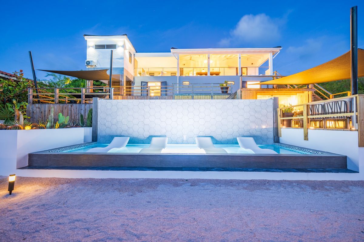Luxe villa met verlicht zwembad en ligstoelen. Sfeervol uitzicht tijdens het blauwe uur.