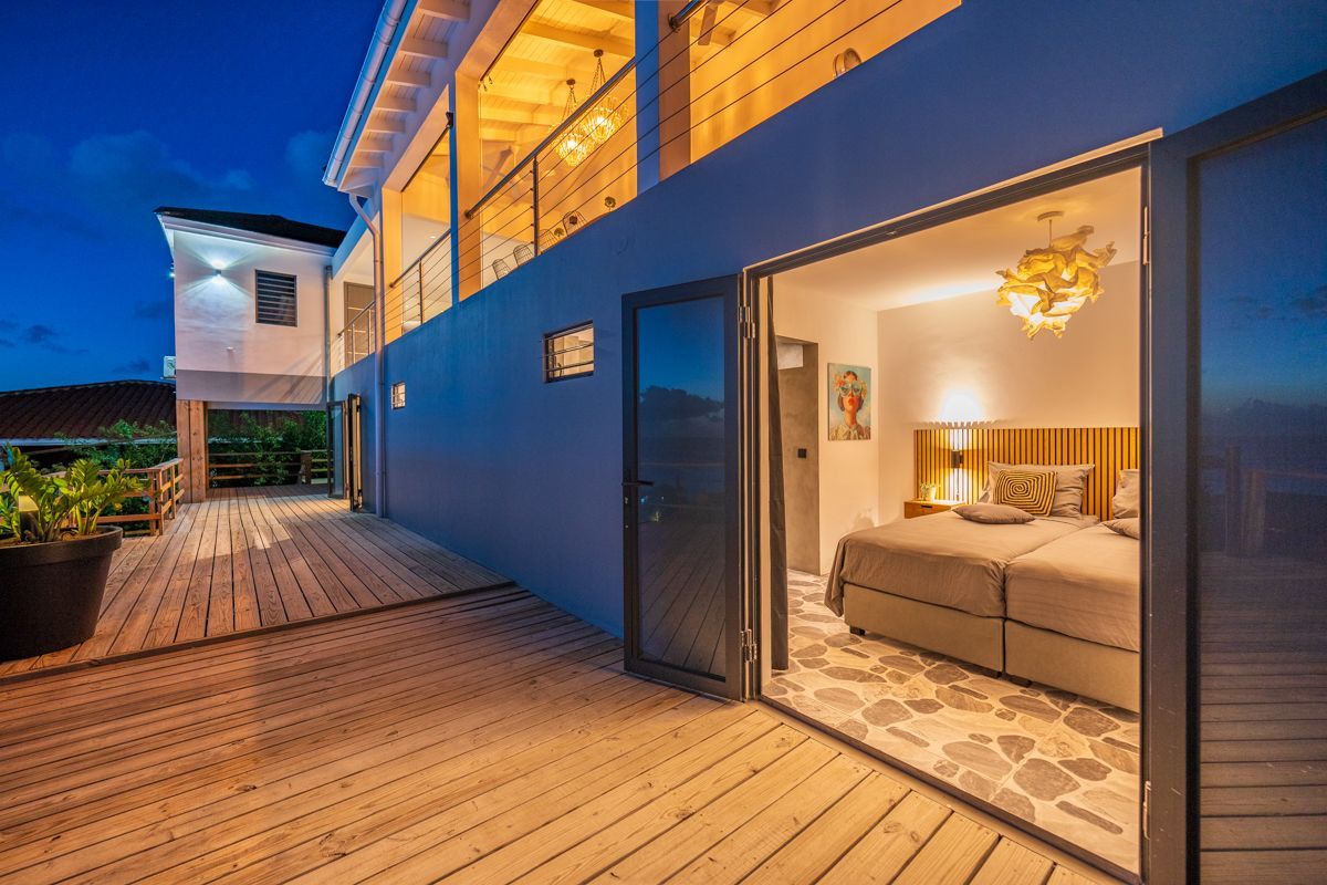 Exterieurzicht van een modern gebouw 's nachts. Open deuren onthullen een verlichte slaapkamer. Houten terras.