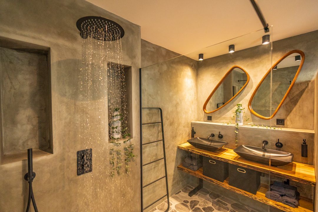 Moderne badkamer met betonnen muren, regendouche, twee wastafels en houten planken.