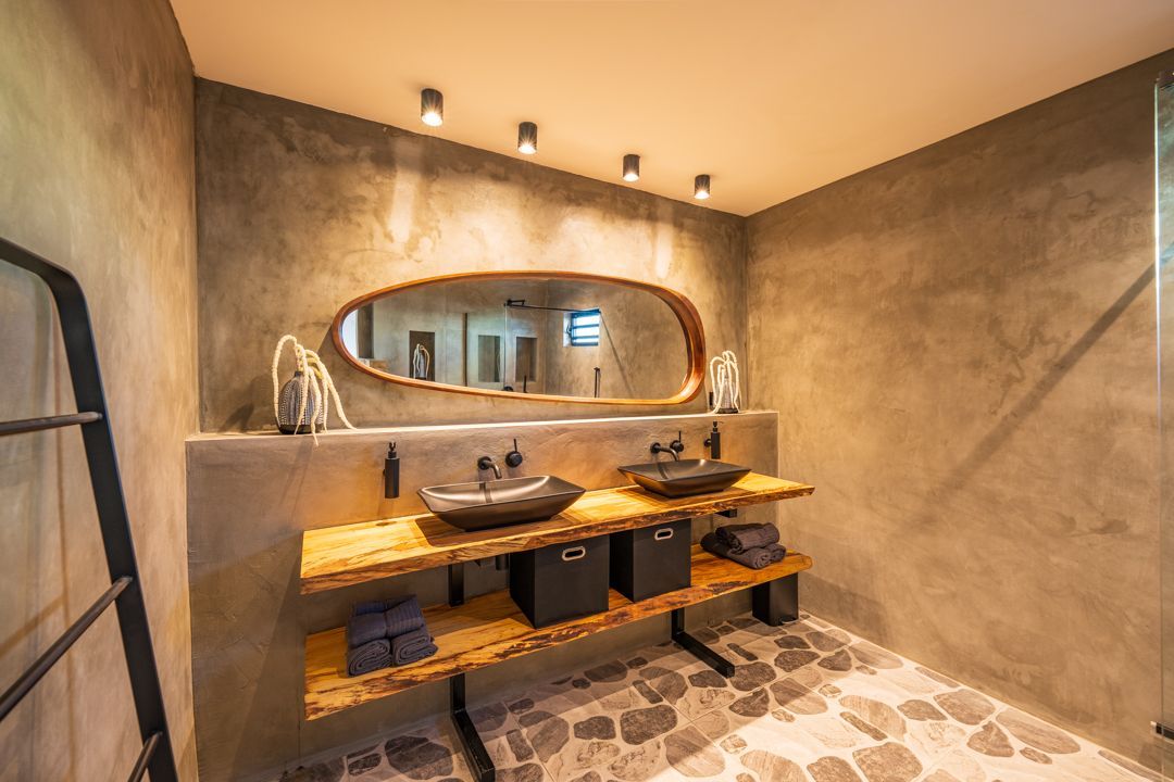 Moderne badkamer met stenen vloer, dubbele wastafel, houten planken en betonnen muren.