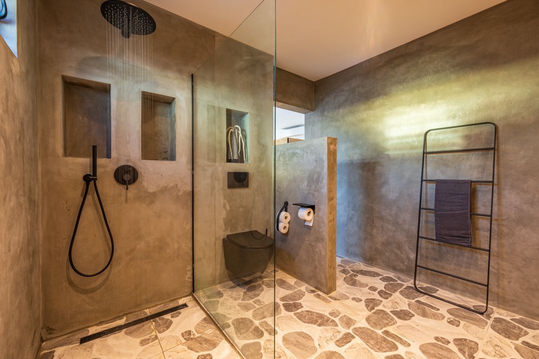 Moderne badkamer met stenen vloer, betonnen muren, glazen douchecabine en zwarte armaturen.