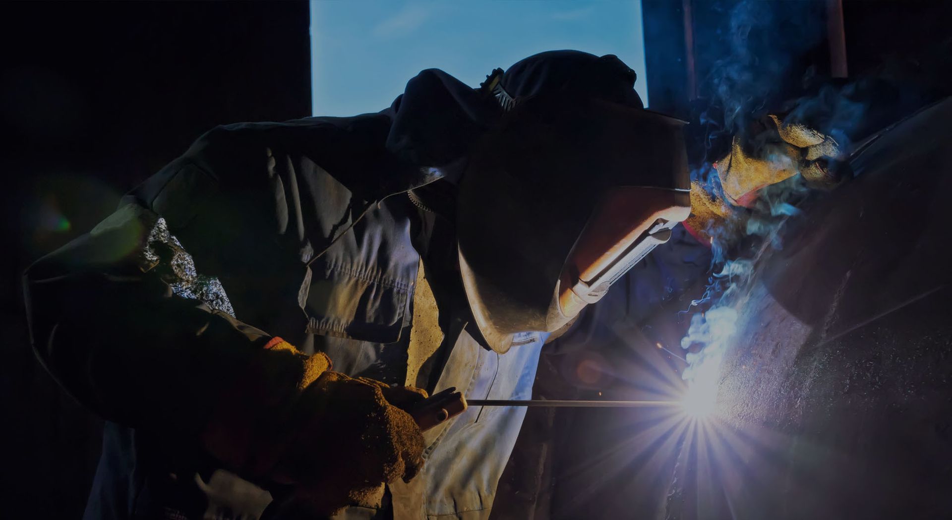 A man is welding a piece of metal in a dark room.