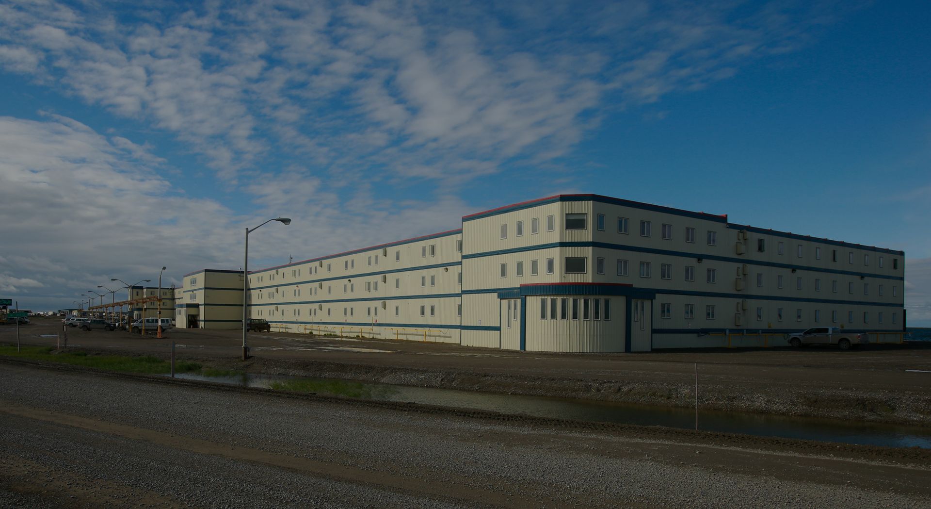 A large building with a lot of windows is sitting on top of a gravel road.