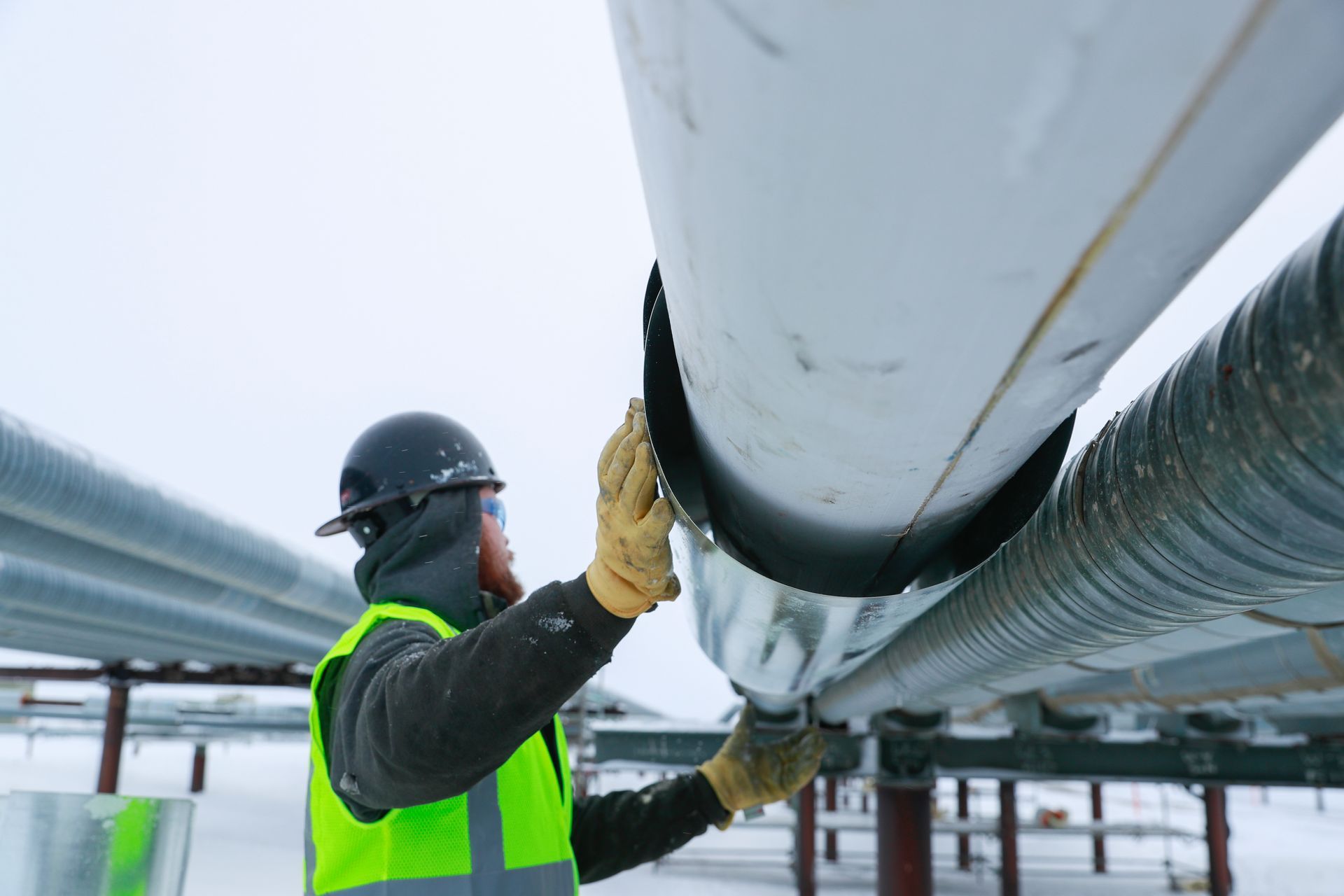 A man is working on a pipe in the snow.