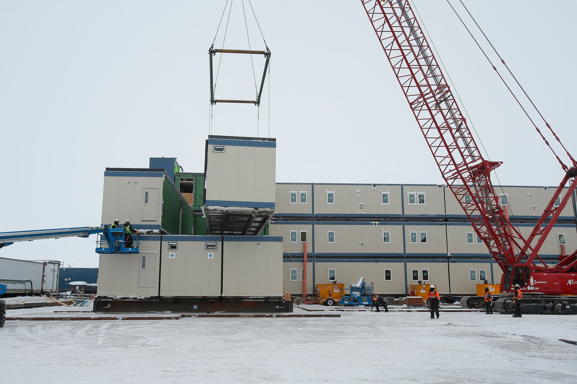 A large red crane is lifting a building in the snow