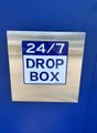 24/7 drop box sign on a stainless steel box against a blue wall