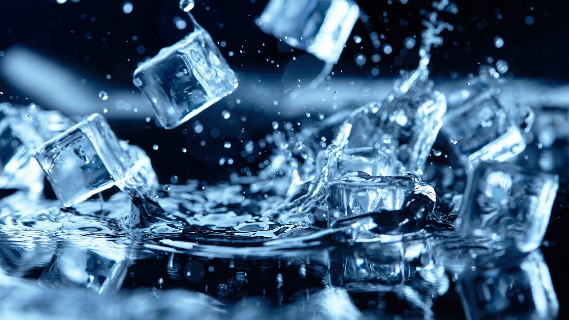 Close-up of clear ice cubes splashing into dark water with bright blue highlights