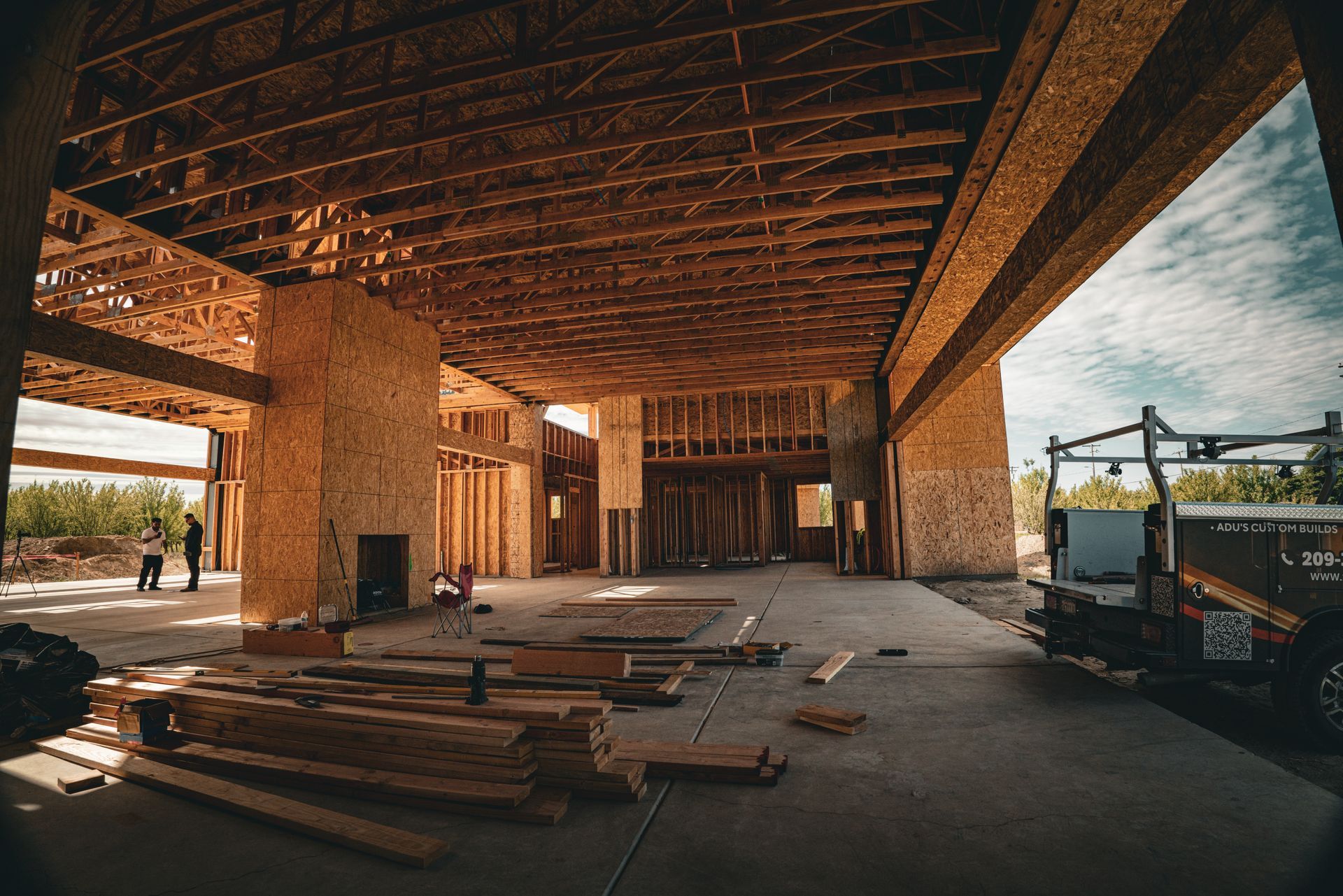 Partially built wooden interior with exposed beams, stacked lumber, and construction equipment near large openings
