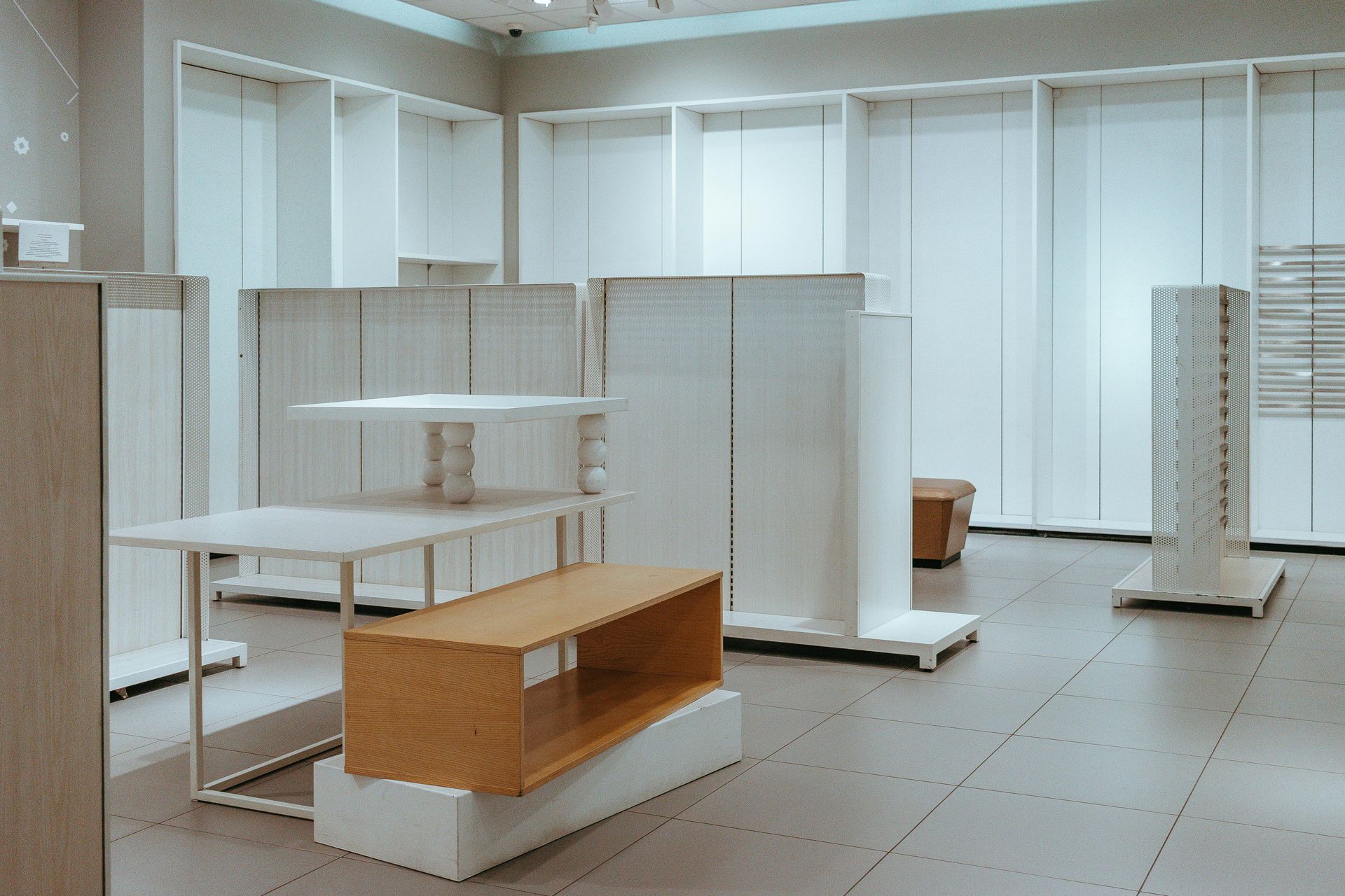 Empty retail store interior with white shelving and a wooden display table on a tiled floor